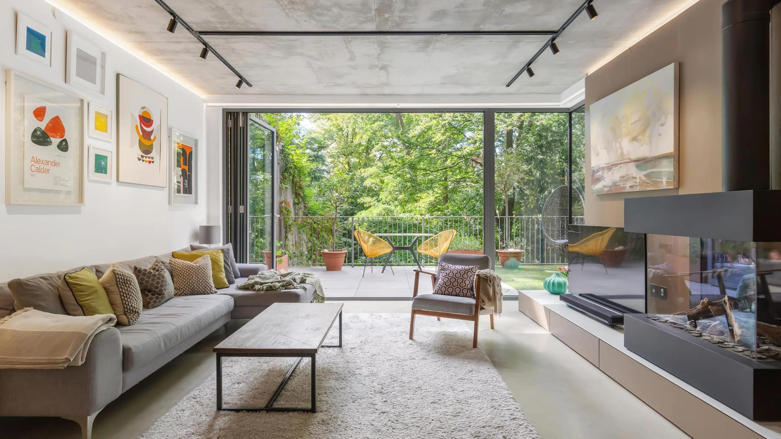Living room with concrete ceiling and floor, neutral sofa with coffee table facing a tv and electric fire