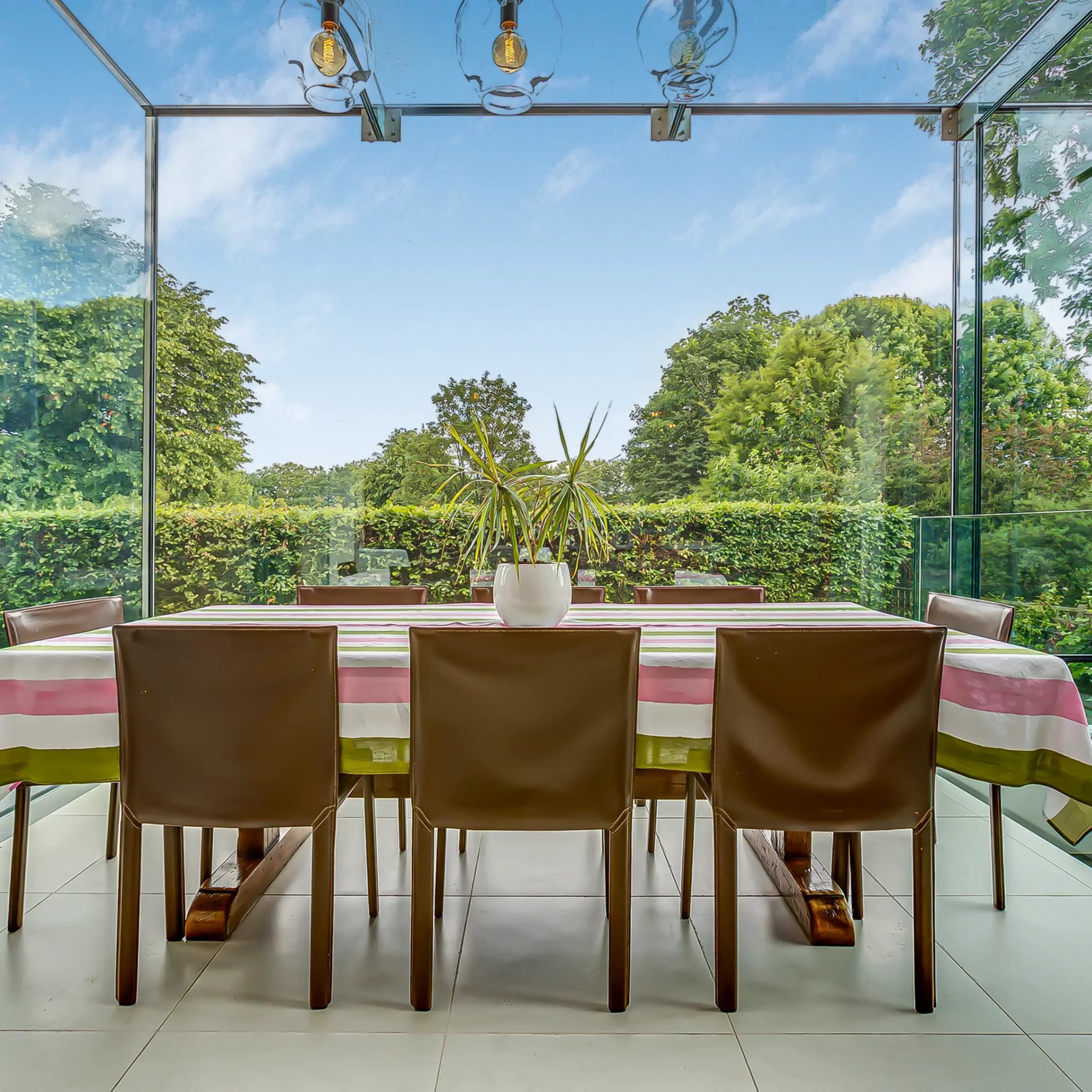Dining area with arm chairs and dining table against an architecturally unique wall made out of glass