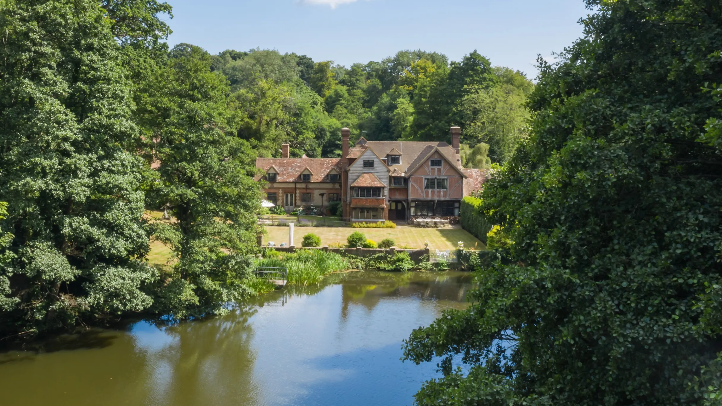 Exterior of large period homes surrounded by tress with a garden leading to a river