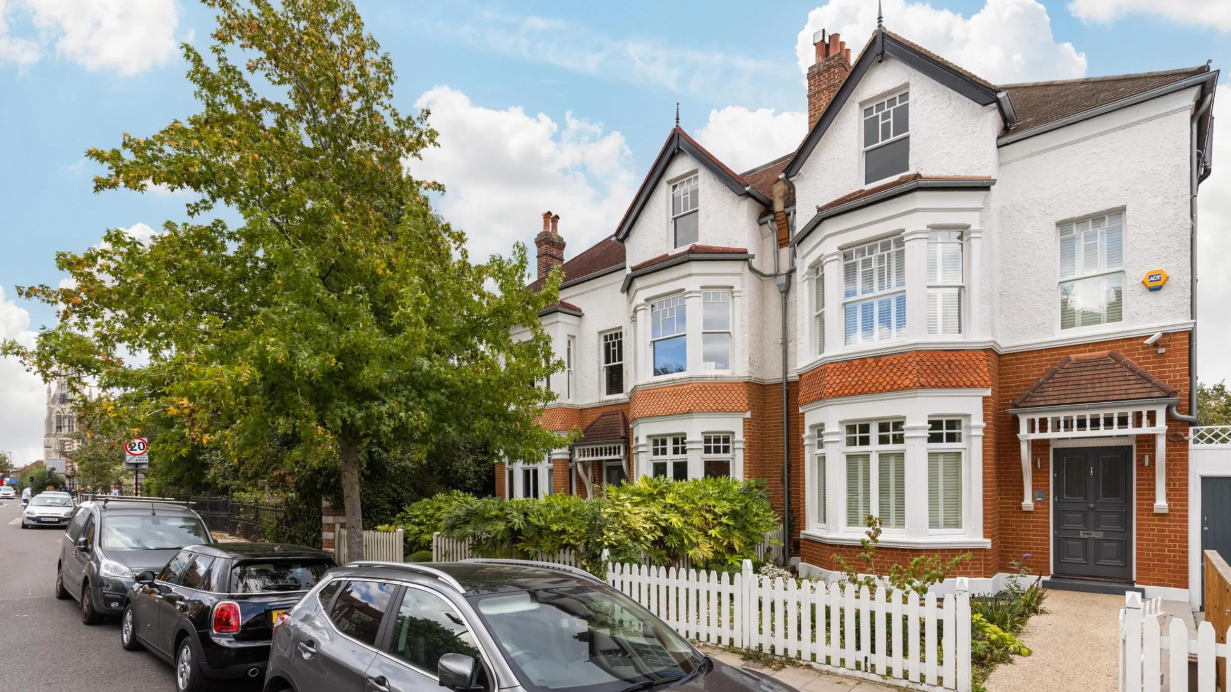 Exterior of Edwardian property with red bricks and white fence, with trees and cars in front