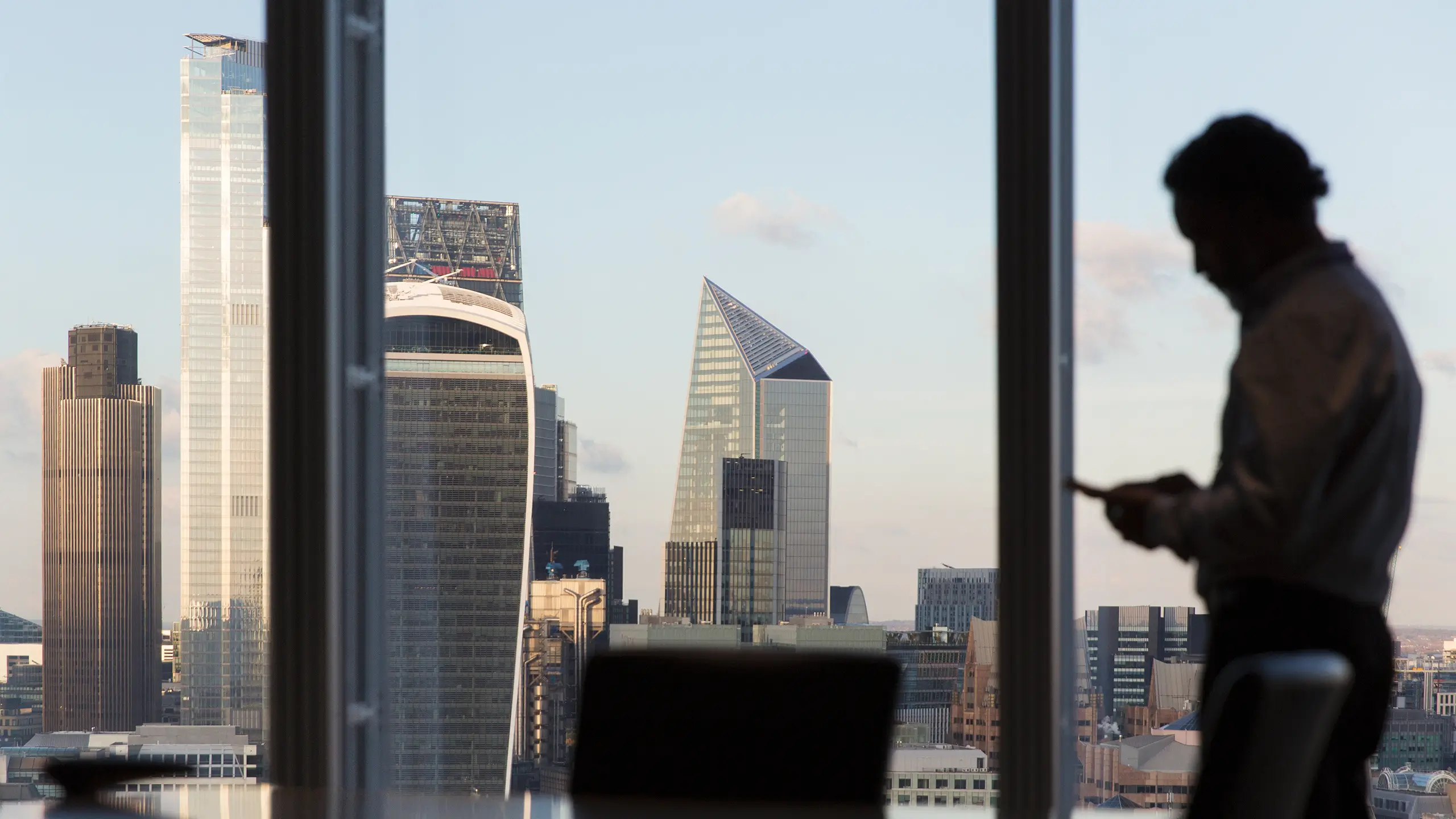 Silhouette corporate businessman using smart phone at highrise office window with city view, London, UK